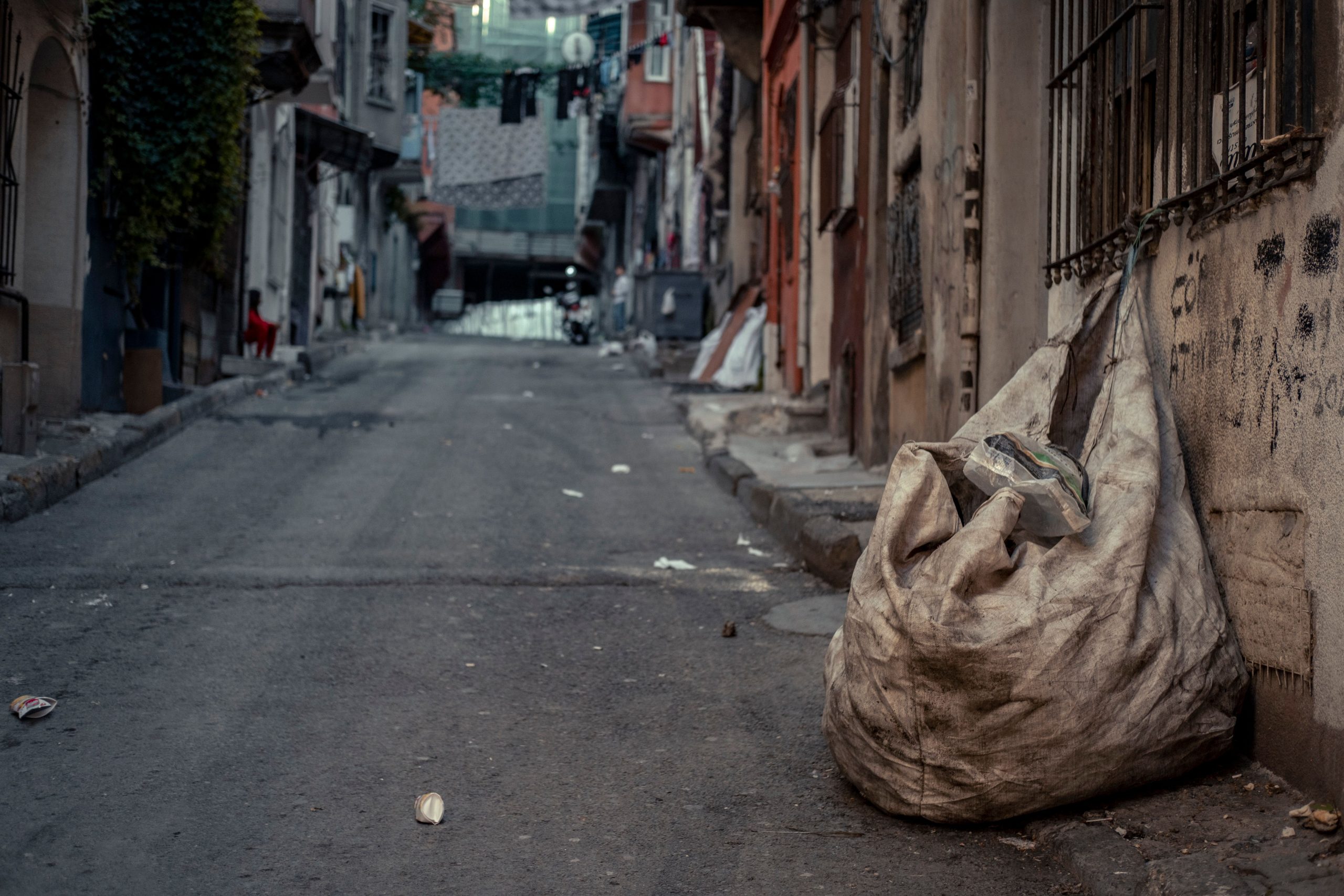 Narrow street in an old town featuring a large bag of garbage with urban decay elements.