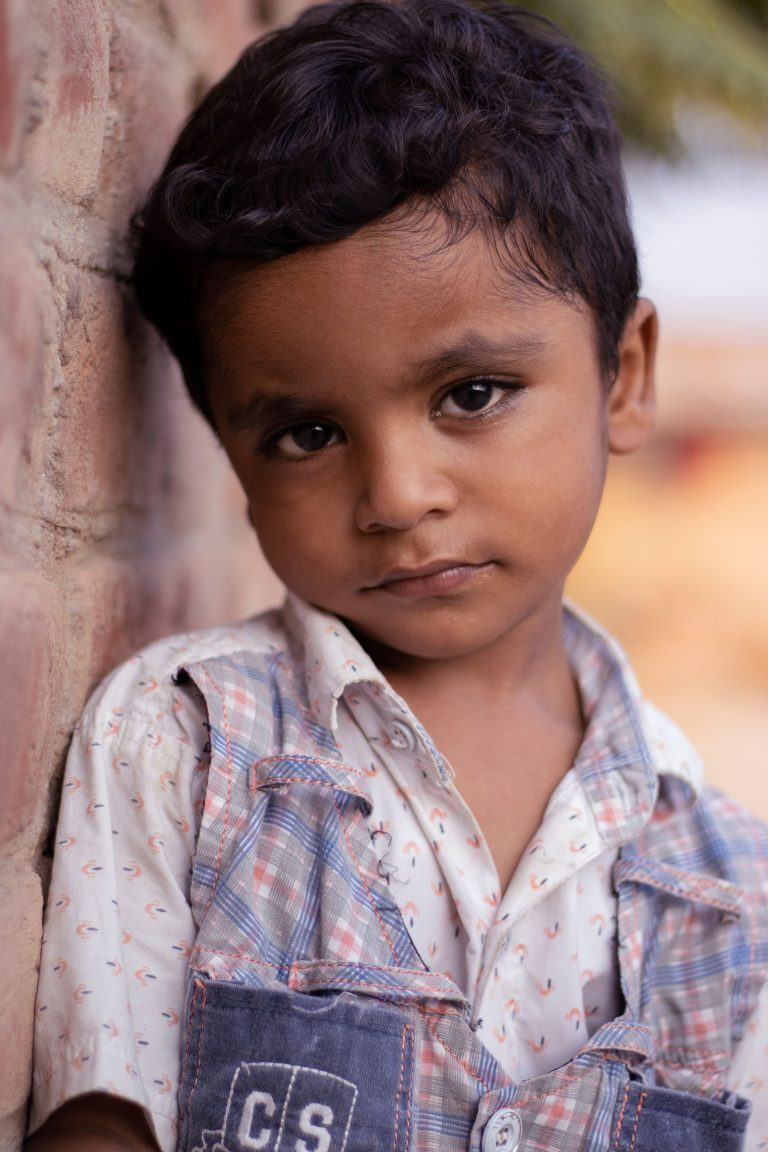 Heartfelt portrait of a young boy leaning against a brick wall, capturing a moment of innocence and reflection.